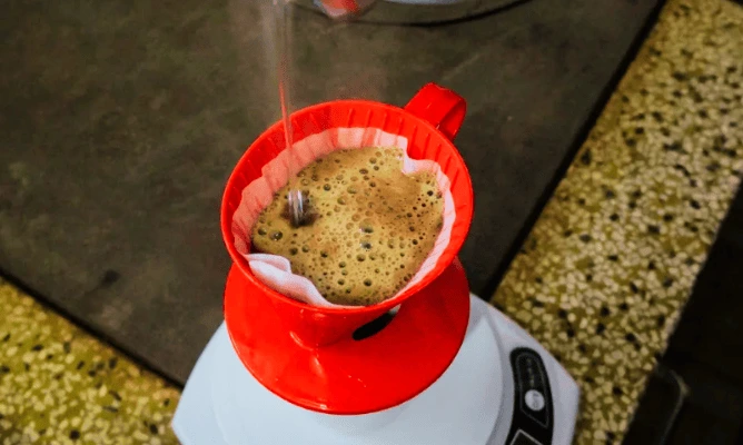 coador Melitta de plástico passando café, abaixo uma balança, sobre uma bancada de cozinha