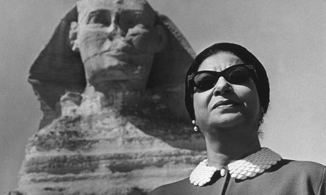 Oum Kalthoum usando óculos escuros, diante de uma esfinge.