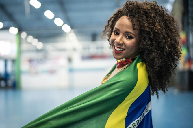 mulher negra, sorridente, enrolada numa bandeira do Brasil