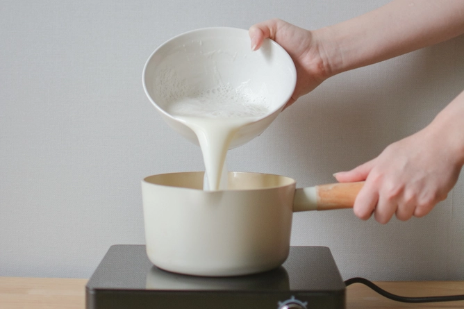 uma panela sobre um fogão de indução e acima dela a pessoa está despejando o leite para aquecer