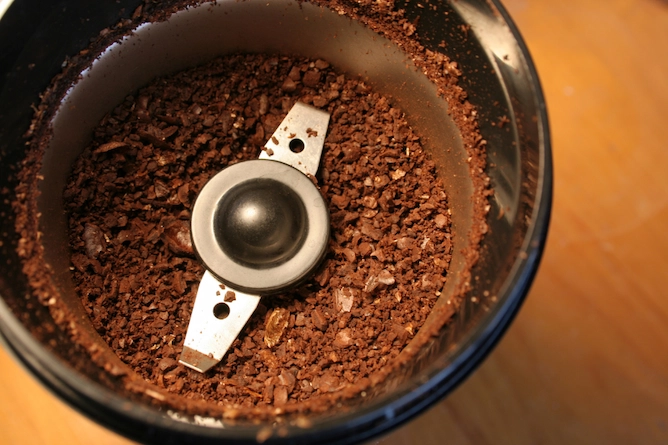 moedor de café, redondo, tem lâminas de metal e grãos de café grosseiramente moídos dentro