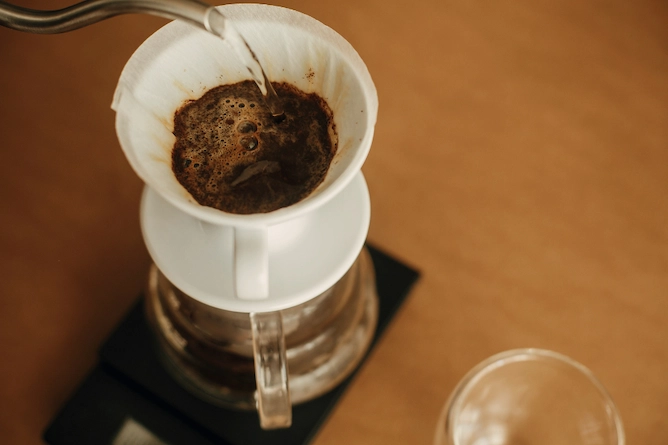 sobre uma mesa de madeira, uma balança e um passador de café de vidro, passando café com o coador v60 de cerâmica