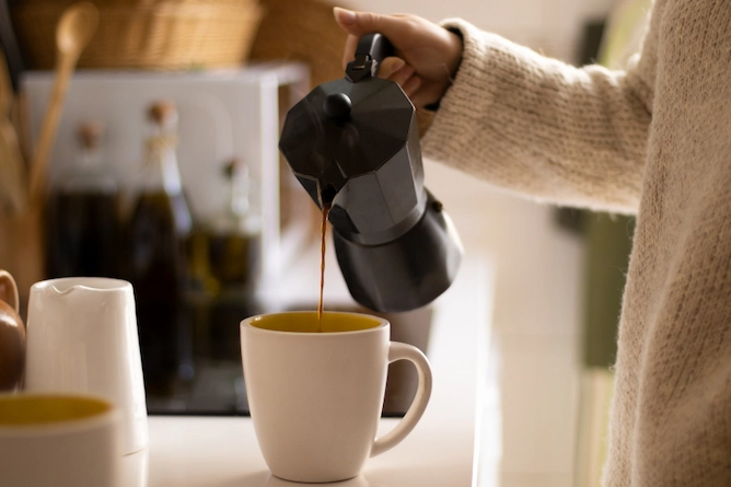 em uma cozinha, uma pessoa serve em uma caneca de porcelana com uma cafeteira italiana