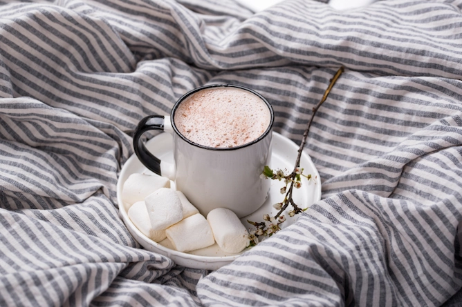 em cima de um pano, um prato de cerâmica com Marshmallow e a xícara com a mistura de café cremoso com chocolate