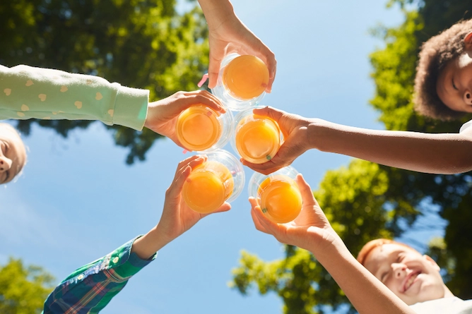cinco crianças brindando com suco de laranja ao ar livre