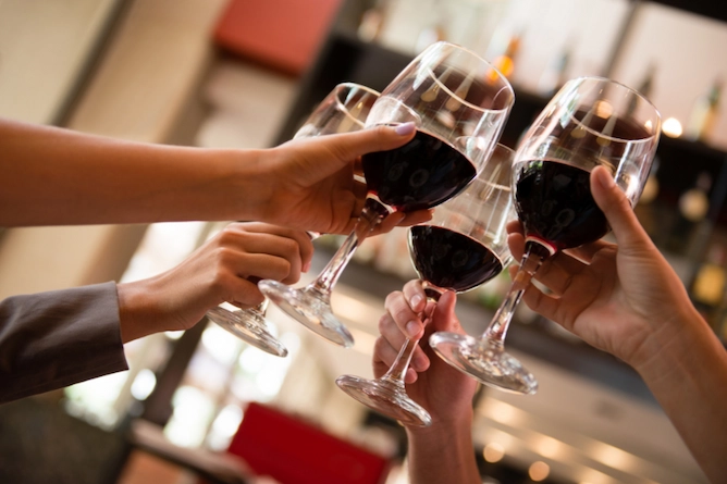quatro pessoas brindando com taças de vinho tinto
