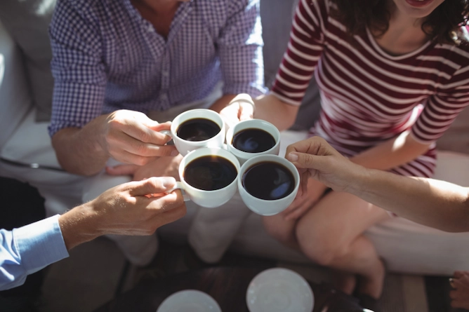 quatro pessoas brindando com xícaras de café passado, sentadas em um sofá
