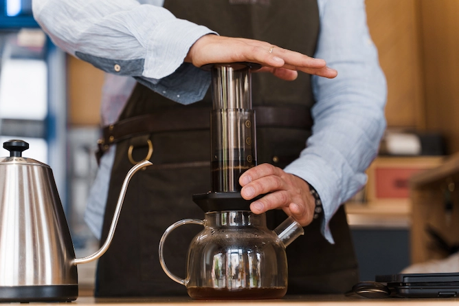 pessoa passando café na aeropress já apertando o êmbulo para passar para um bule