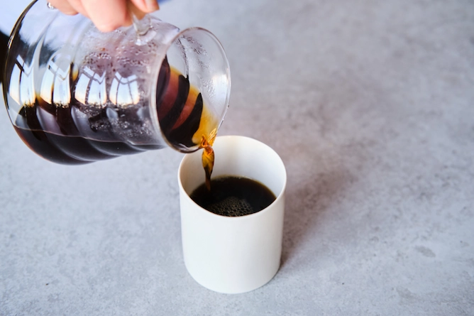 recipiente de vidro servindo café em caneca sobre mesa